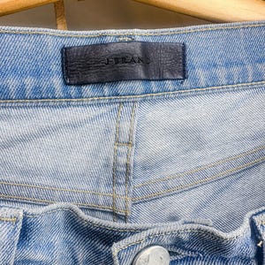May include: Close-up of light blue denim jeans. The jeans feature a black leather tag with the brand name "J BRAND". The jeans have a button closure and visible stitching.