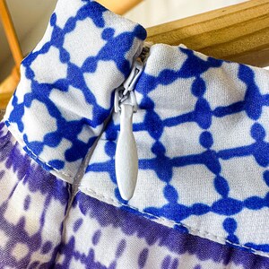 May include: Close-up of a garment with a blue and white geometric pattern. The fabric is a light, airy material. A white zipper is visible, partially open. The garment appears to be a skirt or dress.