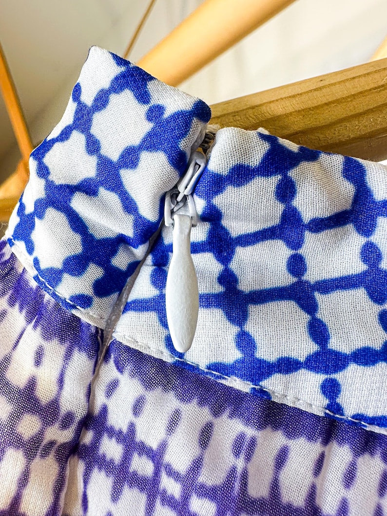 May include: Close-up of a garment with a blue and white geometric pattern. The fabric is a light, airy material. A white zipper is visible, partially open. The garment appears to be a skirt or dress.