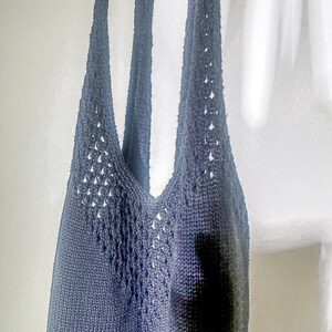 Puede incluir: Un top de tirantes de crochet azul oscuro con un delicado patr&oacute;n de calado. El top tiene un escote en V y tirantes finos.