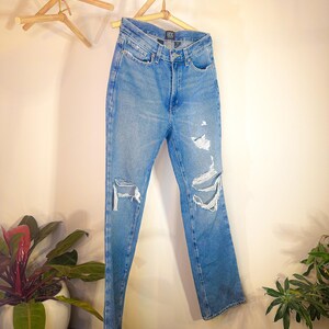 Op de afbeelding: Lichtblauwe denim jeans met distressed details en een rechte pijp. De jeans hangen aan een houten hanger.
