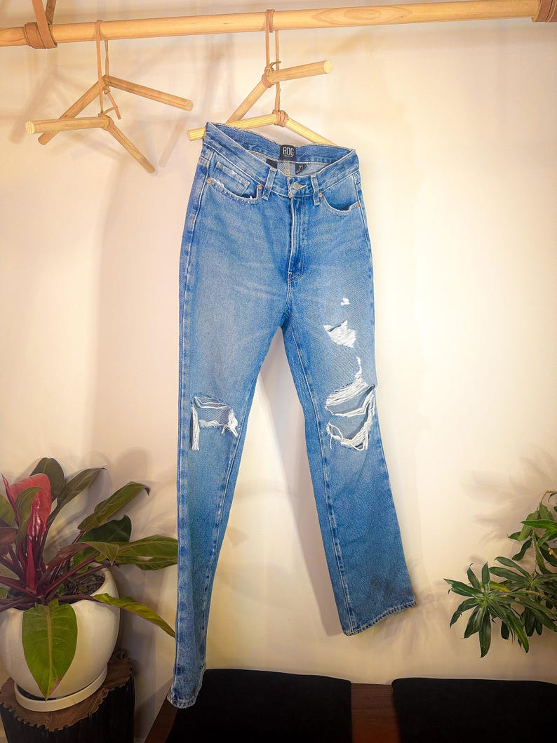Op de afbeelding: Lichtblauwe denim jeans met distressed details en een rechte pijp. De jeans hangen aan een houten hanger.