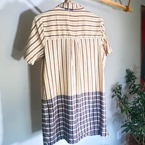 Op de afbeelding: Een shirt met korte mouwen met een gestreept patroon in bruin en beige. De onderste helft van het shirt is een ruitpatroon in blauw, bruin en wit.