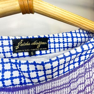 May include: Close-up of a blue and white patterned fabric with a purple and white checkered design. The fabric is labeled "Geisha designs" and "Made in India". The garment is size 6.