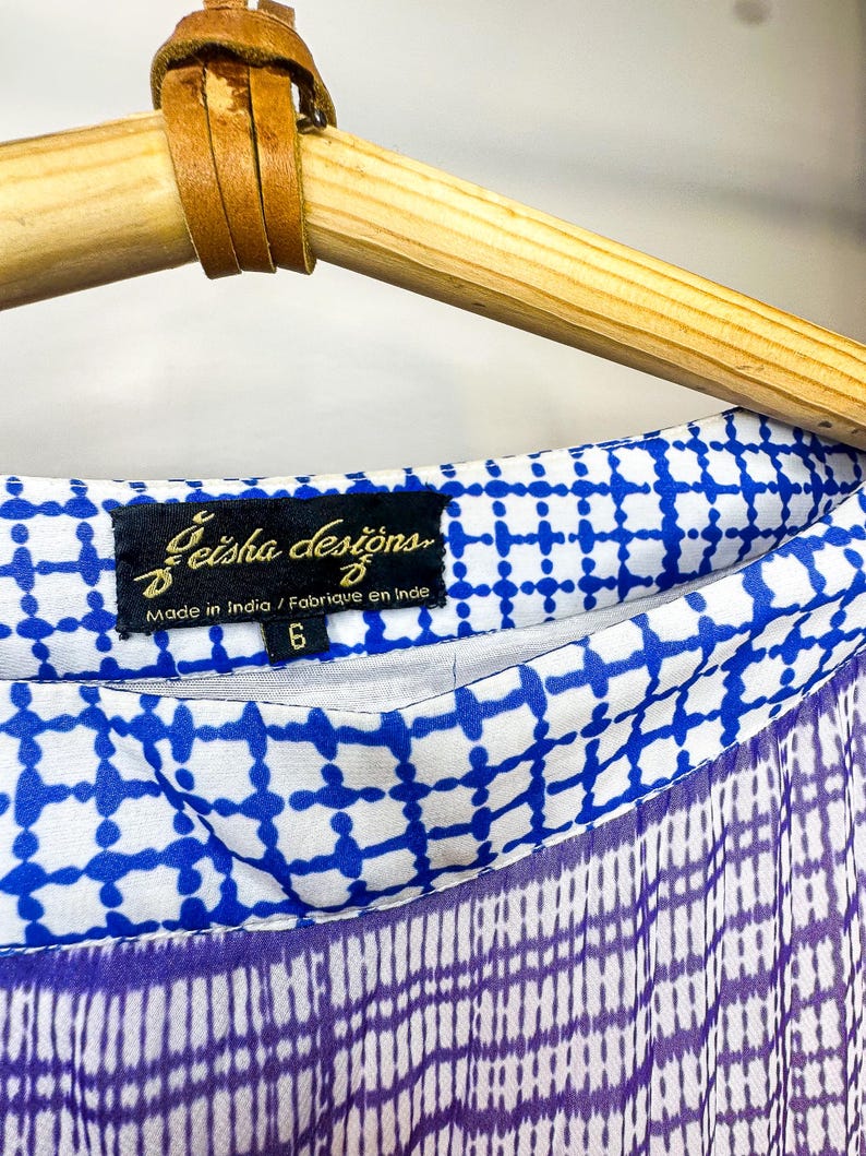 May include: Close-up of a blue and white patterned fabric with a purple and white checkered design. The fabric is labeled "Geisha designs" and "Made in India". The garment is size 6.