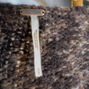 May include: A brown and white fuzzy sweater with a Free People tag attached. The tag is made of metal and has the words "Free People" written on it.