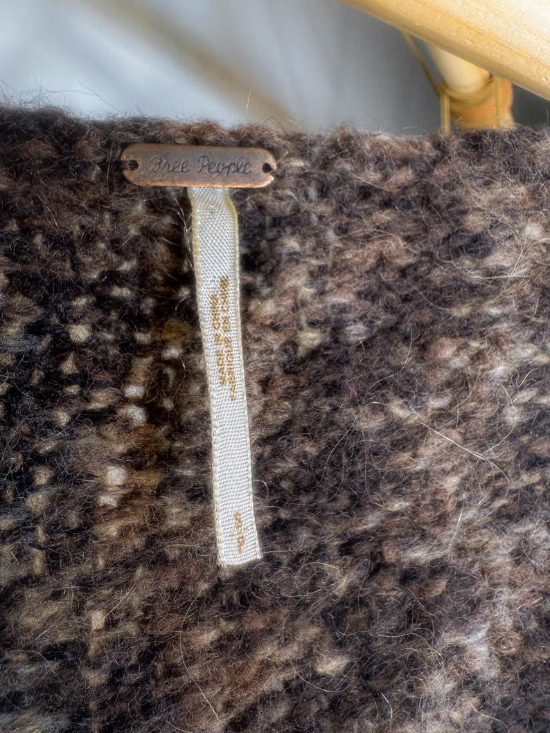 May include: A brown and white fuzzy sweater with a Free People tag attached. The tag is made of metal and has the words "Free People" written on it.