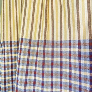Op de afbeelding: Een stof met een gestreept patroon in bruin en beige, overgaand in een geruit patroon in blauw, rood en wit.