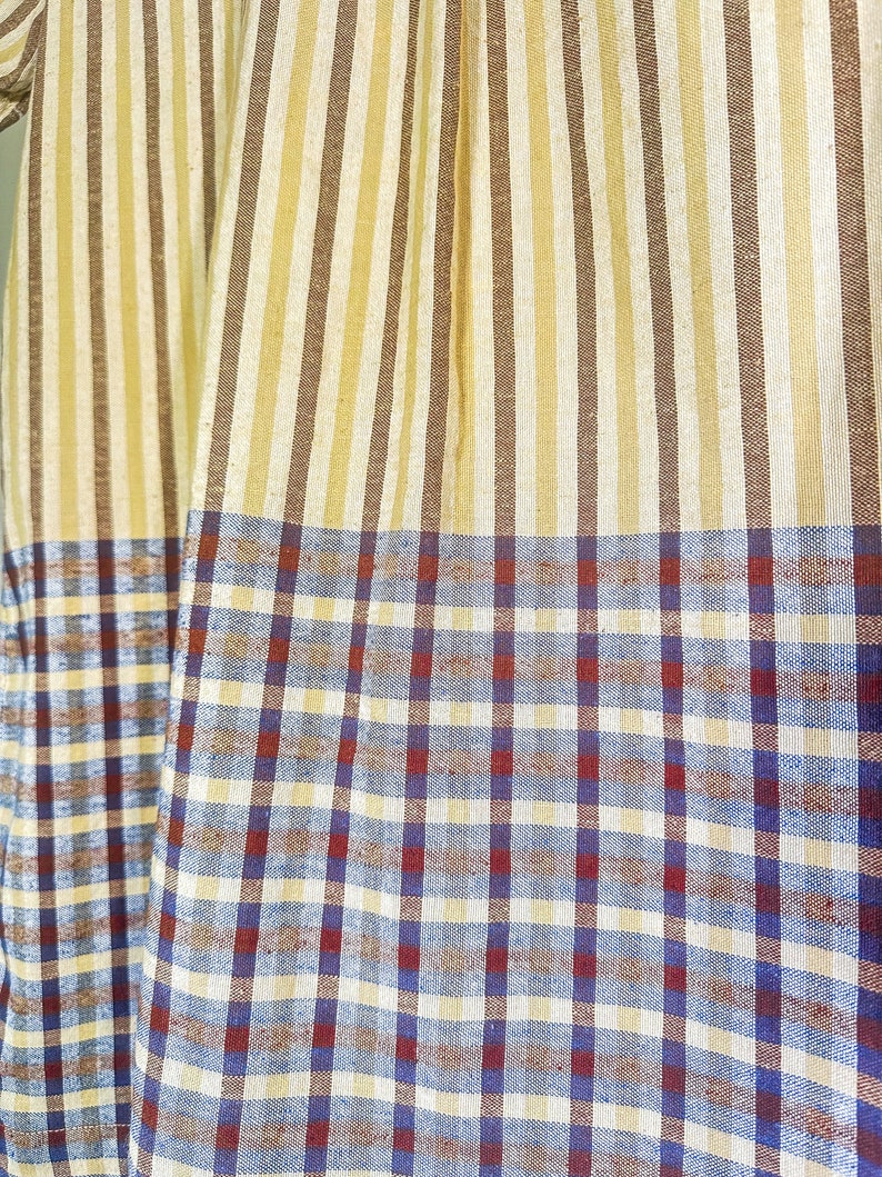Op de afbeelding: Een stof met een gestreept patroon in bruin en beige, overgaand in een geruit patroon in blauw, rood en wit.