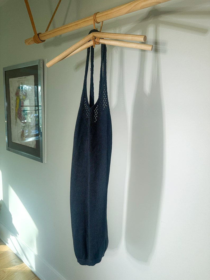 Puede incluir: Un top de tirantes de punto azul oscuro colgado de una percha de madera.
