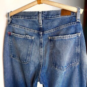 Op de afbeelding: Een paar blauwe denim jeans met een bruin leren patch met de tekst "Bdg" op de achterkant van de tailleband.