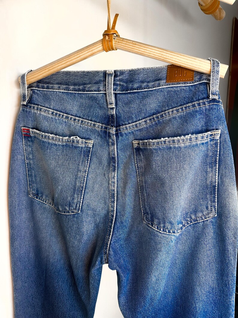 Op de afbeelding: Een paar blauwe denim jeans met een bruin leren patch met de tekst "Bdg" op de achterkant van de tailleband.