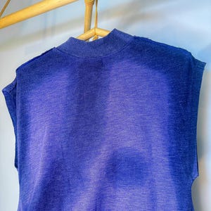 May include: A sleeveless shirt in a gradient of blue shades, hanging on a wooden hanger.
