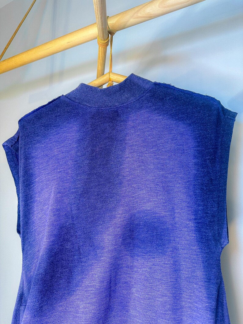 May include: A sleeveless shirt in a gradient of blue shades, hanging on a wooden hanger.