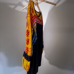 Puede incluir: Una blusa negra de manga larga con un dise&ntilde;o bordado floral amarillo, rojo, rosa y azul en las mangas y el escote.