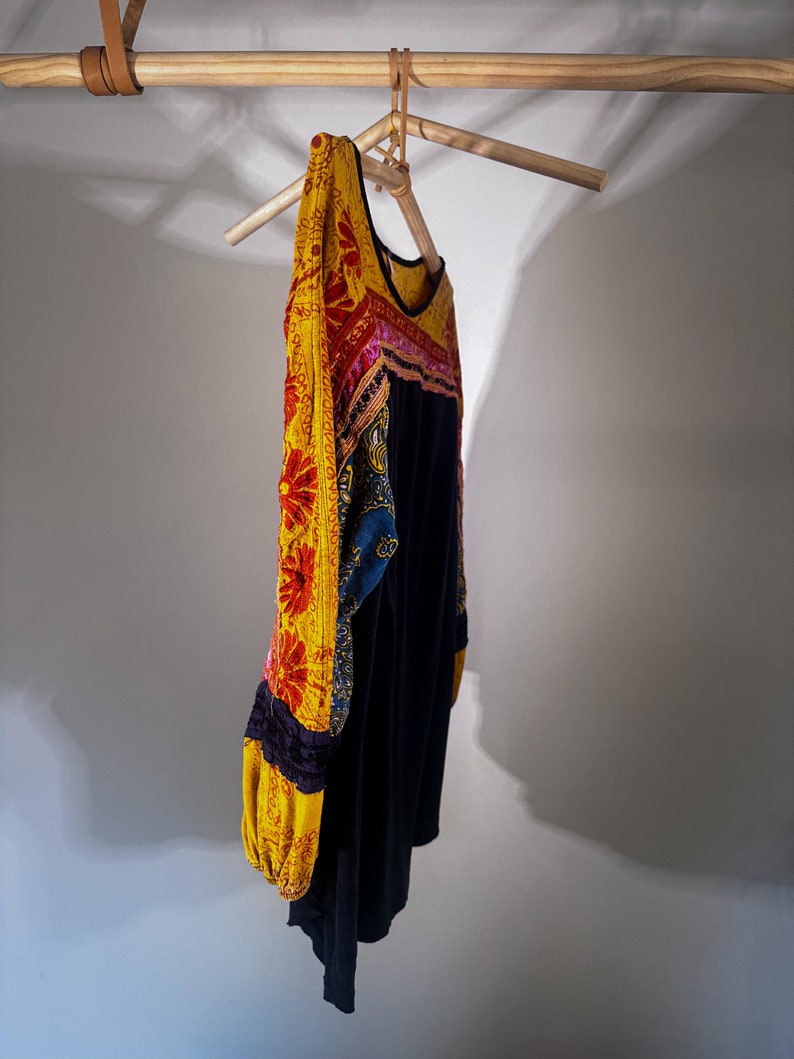 Puede incluir: Una blusa negra de manga larga con un dise&ntilde;o bordado floral amarillo, rojo, rosa y azul en las mangas y el escote.