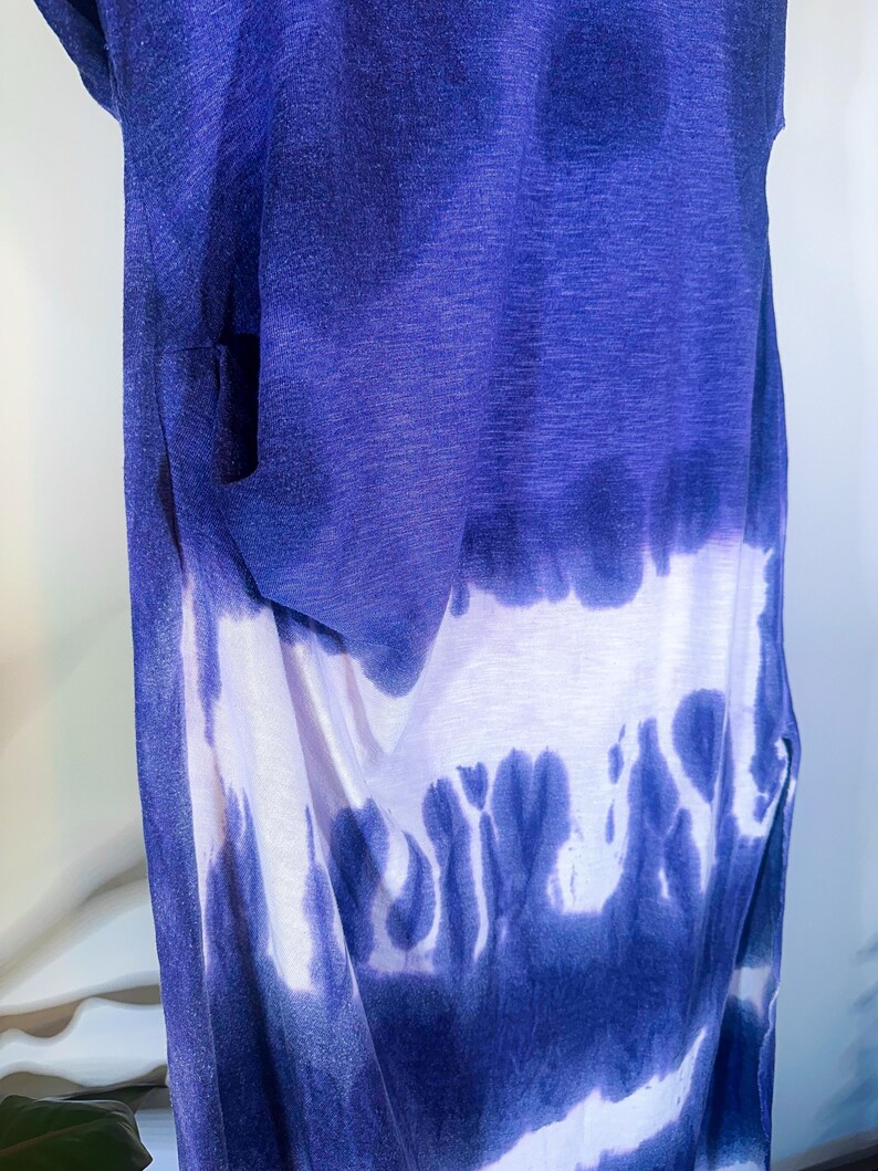 May include: A sleeveless tie-dye dress with a blue and white ombre pattern. The dress is made of a soft, lightweight fabric and has a relaxed fit.