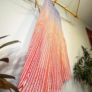 May include: A flowing, pleated skirt with a vibrant gradient design. The skirt transitions from a deep red at the bottom to orange and then to blue at the top. The pattern is a series of vertical red lines on a white background.
