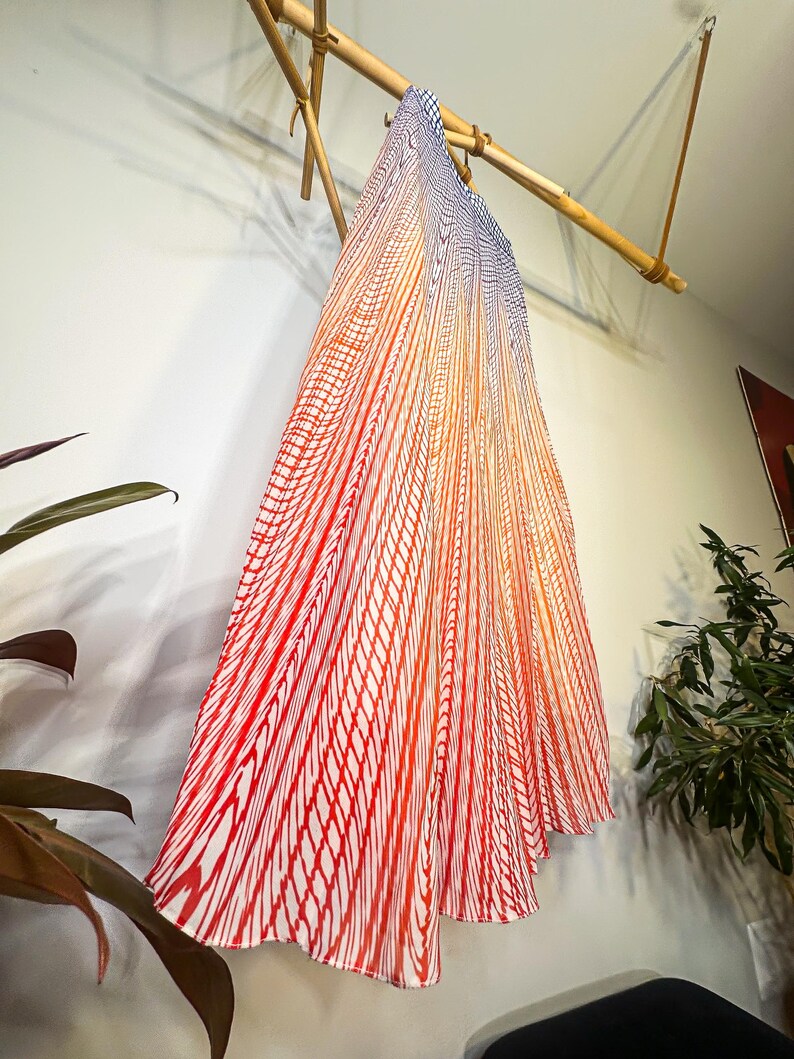 May include: A flowing, pleated skirt with a vibrant gradient design. The skirt transitions from a deep red at the bottom to orange and then to blue at the top. The pattern is a series of vertical red lines on a white background.