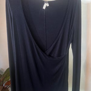 Puede incluir: Camiseta negra de manga larga con cuello en V profundo y detalle de envoltura. La camiseta tiene una etiqueta de talla que dice "M+M" y "M".