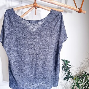 May include: A gray and white heather knit t-shirt with a scoop neck and short sleeves hanging on a wooden hanger.