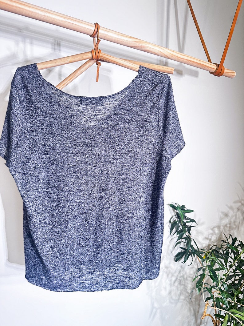 May include: A gray and white heather knit t-shirt with a scoop neck and short sleeves hanging on a wooden hanger.