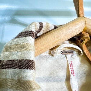 Op de afbeelding: Een gestreept bruin en wit shirt met een Free People-label met de tekst "Made in India, Fabrique en Inde".