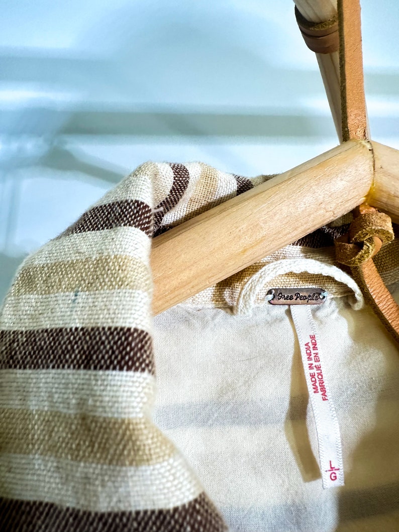 Op de afbeelding: Een gestreept bruin en wit shirt met een Free People-label met de tekst "Made in India, Fabrique en Inde".