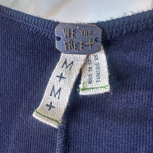 Puede incluir: Un top de tanque negro de canal&eacute; con una etiqueta We The Free+ y una etiqueta de talla M.