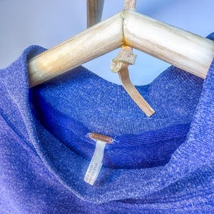 May include: A blue, soft, knit sweater with a cowl neck. The sweater has a tag that reads "Made in India / Fabriqu&eacute; en Inde".