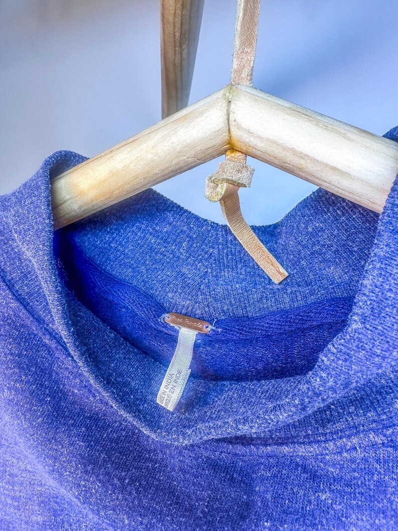 May include: A blue, soft, knit sweater with a cowl neck. The sweater has a tag that reads "Made in India / Fabriqu&eacute; en Inde".