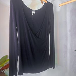 Puede incluir: Camiseta negra de manga larga con escote cruzado. La camiseta est&aacute; hecha de un tejido suave y el&aacute;stico.