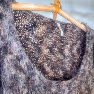 May include: A brown and gray fuzzy sweater with a scoop neck. The sweater is hanging on a wooden hanger.