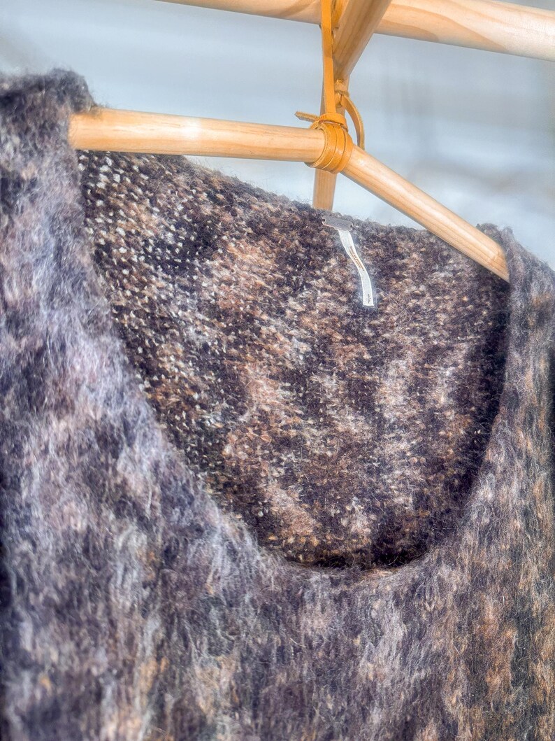 May include: A brown and gray fuzzy sweater with a scoop neck. The sweater is hanging on a wooden hanger.