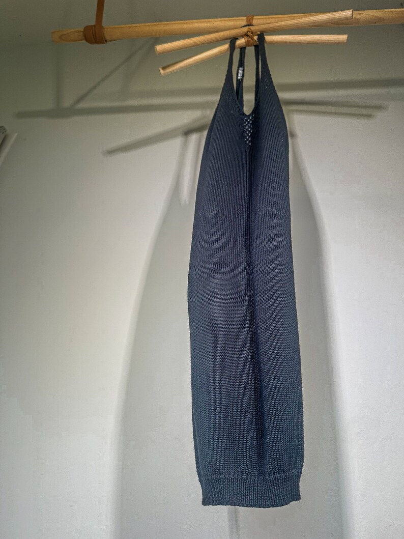 Puede incluir: Un vestido negro de punto sin mangas colgado de una percha de madera.