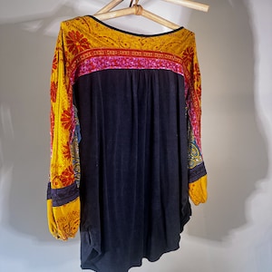 Puede incluir: Una camisa negra de manga larga con un tejido estampado en amarillo, rojo y azul en las mangas y el escote.