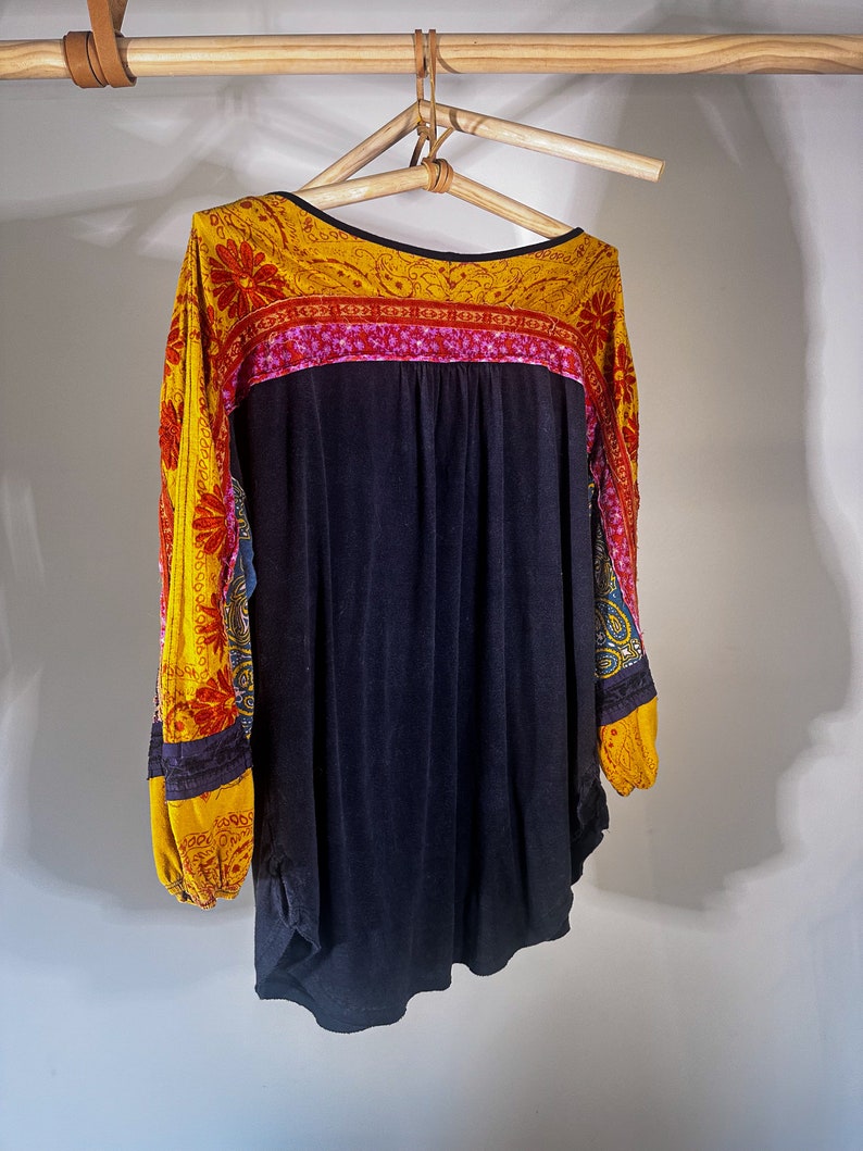 Puede incluir: Una camisa negra de manga larga con un tejido estampado en amarillo, rojo y azul en las mangas y el escote.