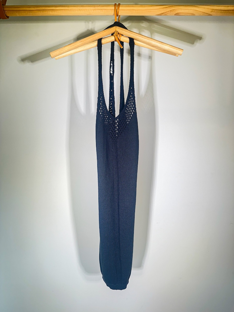 Puede incluir: Un top azul oscuro de tirantes con un dise&ntilde;o de crochet. El top est&aacute; colgado en una percha de madera.