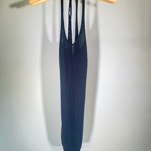 Puede incluir: Un top azul oscuro de tirantes con un dise&ntilde;o de crochet. El top est&aacute; colgado en una percha de madera.