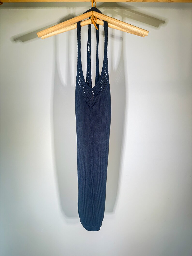 Puede incluir: Un top azul oscuro de tirantes con un dise&ntilde;o de crochet. El top est&aacute; colgado en una percha de madera.