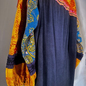 Puede incluir: Una camisa azul oscuro de manga larga con tela estampada de colores en las mangas. Las mangas est&aacute;n hechas de un patchwork de diferentes telas, incluyendo amarillo, rojo, azul y verde.