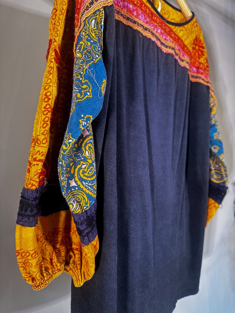 Puede incluir: Una camisa azul oscuro de manga larga con tela estampada de colores en las mangas. Las mangas est&aacute;n hechas de un patchwork de diferentes telas, incluyendo amarillo, rojo, azul y verde.