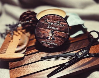 May include: A black jar of Fancy Bear beard balm with a wooden lid and a label featuring a cartoon bear wearing a top hat and bow tie. The label reads "Fancy Bear Beard Balm Lavender Simple, Natural & Organic 1oz".