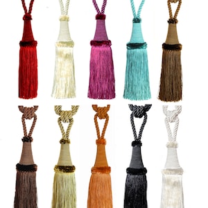 May include: Ten different colours of tassel tiebacks for curtains. The tassels are made of a soft, fluffy material and have a loop at the top for hanging. The colours include red, white, pink, turquoise, brown, beige, orange, black, and white.