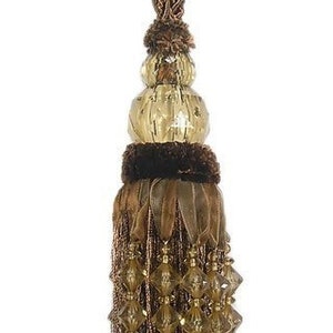 Op de afbeelding: Een bruine en gouden kwast met een kralenrand en een decoratief bovenstuk. De kwast is gemaakt van een geweven stof en heeft een metallic glans.