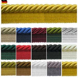 Könnte beinhalten: Eine Auswahl an dekorativen Seilborten in verschiedenen Farben, darunter Gold, Blau, Rot und Grün. Die Borte hat ein gedrehtes Seildesign über einem Fransenrand. Ideal für Polster, Vorhänge und Bastelprojekte.