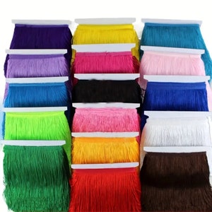 Op de afbeelding: Assortiment van 16 kleuren franjesbies, elke kleur wordt weergegeven op een witte kaart. De franjes zijn ongeveer 2,5 cm breed en hebben een zachte, pluche textuur.