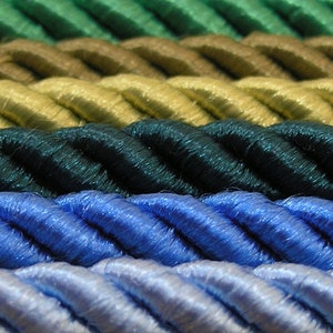 Op de afbeelding: Close-up van een verscheidenheid aan gedraaide touwkoorden in verschillende kleuren, waaronder groen, bruin, geel, blauw en lichtblauw.