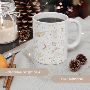 Puede incluir: Taza de cerámica blanca con un diseño dorado de estrellas, lunas y otros símbolos mágicos. La taza está llena de café oscuro y tiene un asa en el lado derecho.