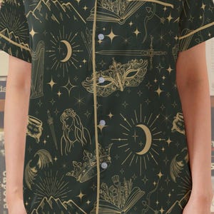 May include: Dark green pajama set with a gold celestial pattern, including moons, stars, mountains, and open books. The set features a button-down shirt with gold trim and matching shorts. The text "FANTASY PJ SET" is visible.